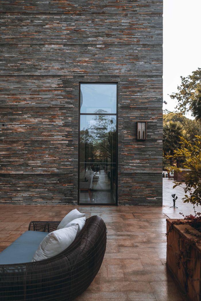 A contemporary patio featuring a wicker couch, glass door, and an elegant stone wall design. Ideal for relaxation.